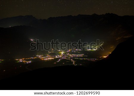 Aerial photo of a quiet small town in a valley that was taken from above on a mountain at nighttime with the road network visible because of the streetlights. 