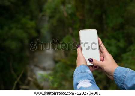 a woman's hand with a manicure takes a photo of the forest landscape. use as a template for your photo.