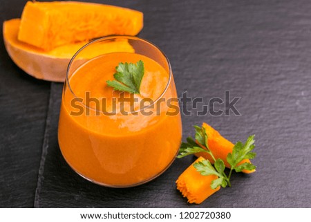 Fresh pumpkin smoothie in glass with parsley on black slate background. Horizontal view. Copy space