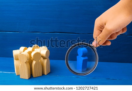 Magnifying glass is looking at the crowd of wooden figures of people stand distantly and look at the blue man. The person tries to establish contact with the group. Good business leader