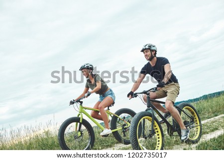 Young couple are cycling on fatbikes at green hills. They are wearing protected equipment