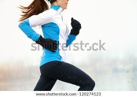 Running athlete woman sprinting during winter training outside in cold snow weather. Close up showing speed and movement.