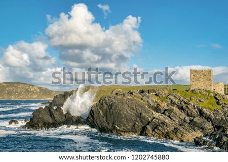 Picture of waves crashing on a rocky coast infront of a castle in Donegal Ireland