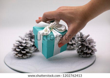 A Christmas gift. Women's hands hold a small jewellery box with a white ribbon. Cones on the background.