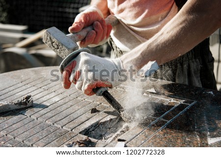 Stone carver in gloves working with a hammer and chisel on a marble slab. heavy handwork. production of monuments from marble. working with natural stone Royalty-Free Stock Photo #1202772328