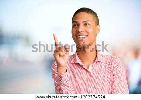 Young african american man pointing with the index finger a great idea and looking up on unfocused outdoor background