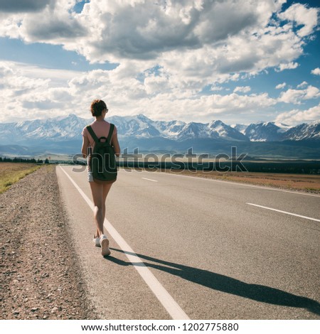 Young woman backpacker walking on road. Mountains at background.