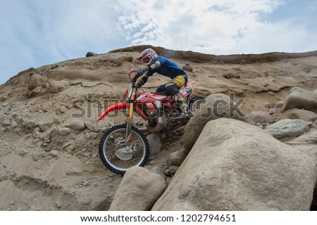 The professional motocross rider on his motorcycle on the extreme rocky terrain trail. Biker climbs a rocky mountain on a motocross motorcycle. Brown tone rocky mountain background