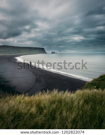 A man walking on a black sand beach, moody cloudy sky in the background, Iceland.  