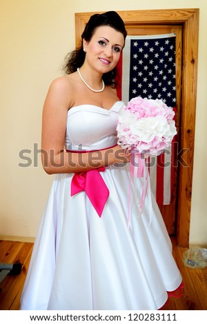 Happy beautiful bride  in white wedding dress with hairstyle and bright makeup on the background of the American flag