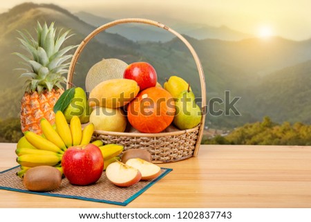 Composition assorted fruits in wicker basket on wooden table, with mist on high mountain in the morning, copy space
