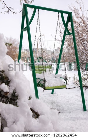 Photo fall of fluffy early white snow on a swing at the playground