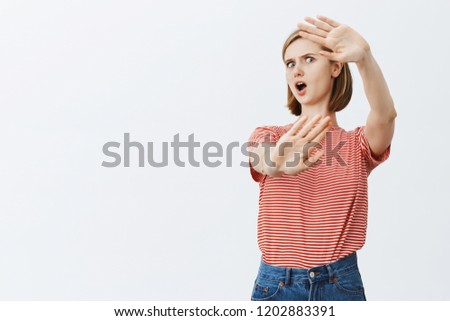 Oh gosh, take it away from me. Displeased intense european girl with short haircut, tilting backwards, pulling palms towards camera to cover face, saying no or rejecting something over grey wall