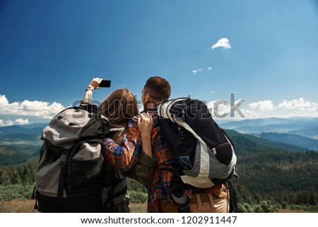 Man and woman standing with focus on back and embracing. Lady holding smartphone for photographing themselves