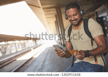 Buy online. Cheerful bearded hindu man sitting on the railway platform while using his credit card
