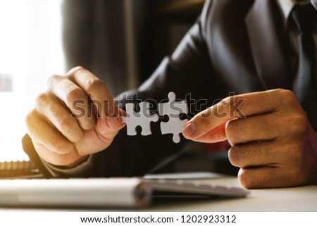 
Business solutions and success concept. Businessman hand connecting jigsaw puzzle at office in morning light