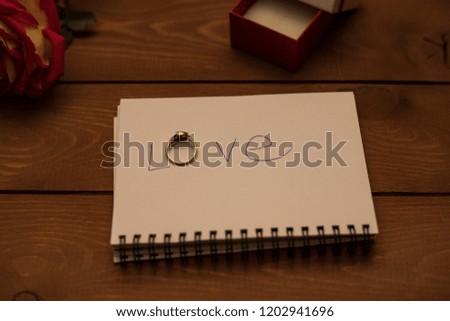 word "love", written on a white paper, red rose and golden ring