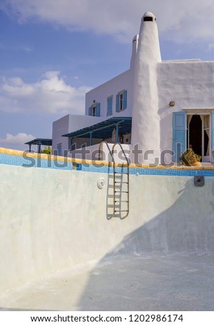 Empty swimming pool with traditional Greek Cycladic island house in the background. 