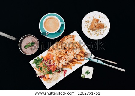 Vertical shot of chicken souvlaki with French fries, pita bread and salad on the side, along with tomato soup, baklava and coffee