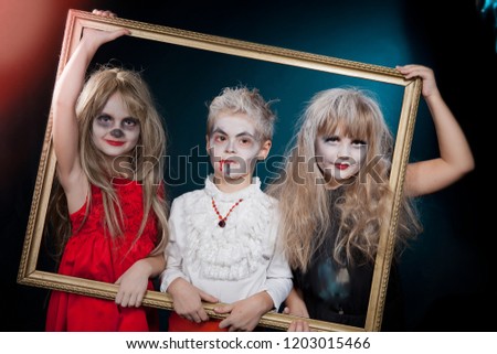 Two girls and boy  wearing  as  vampire and witches for  Halloween posing with antique frame