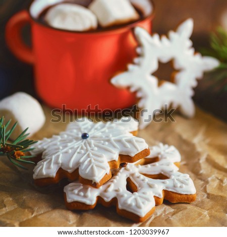 A close-up shot of gingerbread cookies shaped as snowflakes. Hot chocolate or cocoa with marshmallow in red mug.