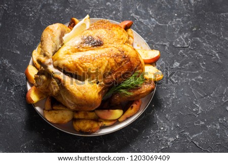 Baked whole chicken with apples on a plate on stone background