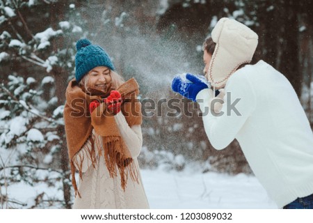 happy young couple playing on winter walk, throwing snowballs and having fun outdoor in snowy forest. Active winter vacation concept.
