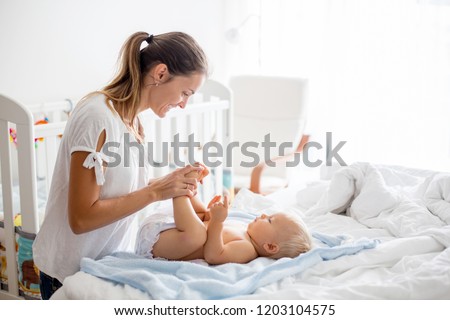 Young mom, changing baby diaper after bath in sunny bedroom