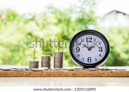 alarm clock and step of coins stacks with tree growing on top, nature background, money, saving and investment or family planning concept, over sun flare silhouette tone.