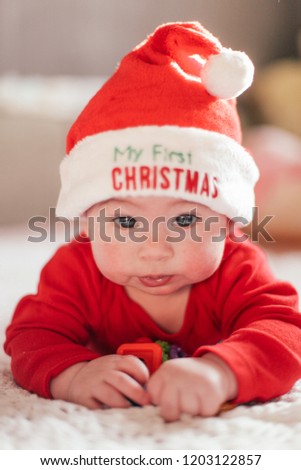A kid in Santa Claus costume with a sign on the hat My first Christams