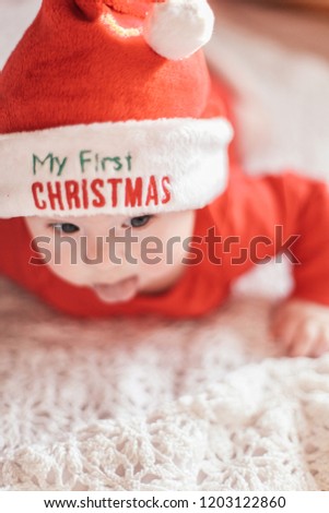 A kid in Santa Claus costume with a sign on the hat My first Christams
