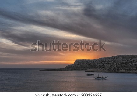 Picture of dramatic sea sunset with boats and rocks.