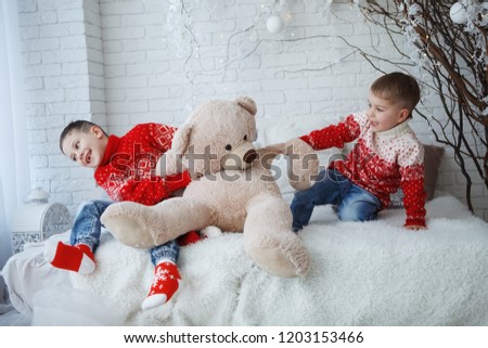 Two brothers Boy in a Christmas red sweater with a picture of a deer sitting on a bed with pillows.