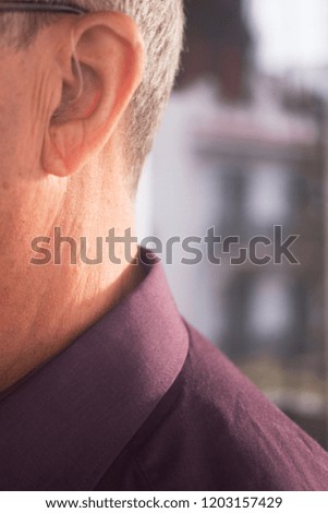 Deaf senior citizen man wearing modern digital high technology hearing aid in ear.
