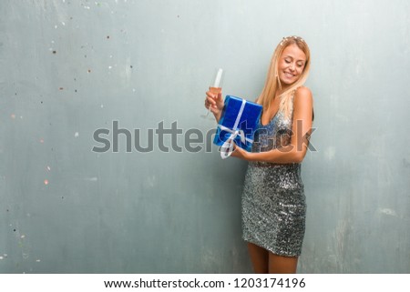 Elegant young blonde woman celebrating new year with champagne, one gift and confetti.