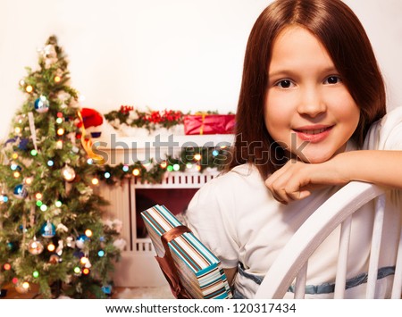 Calm positive girl sitting with present with new year tree on background