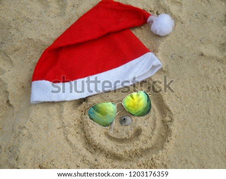 Santa hat with sunglasses are lying on the sand on the beach.