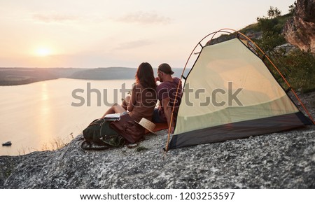Photo of happy couple sitting near tent with a view of lake during hiking trip. Travel Lifestyle adventure vacations concept.