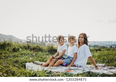 Charming young mother has fun with her little sons lying on a plaid on green grass