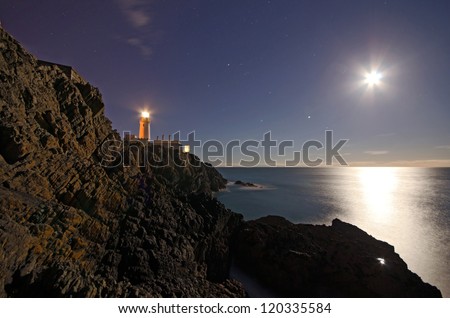 Lighthouse on top of cliffs with night sky, stars and full Moon reflecting in the Sea on the Isle of Man Royalty-Free Stock Photo #120335584