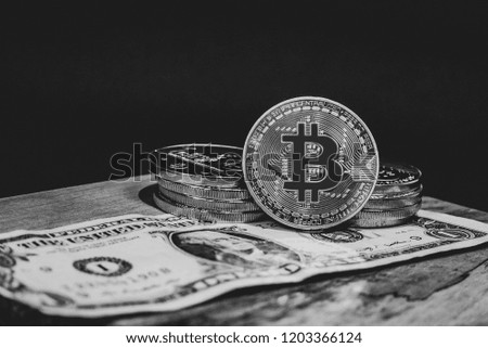 Black and white image of Bitcoin coins on an American Dollar bill on a wooden surface with a black background