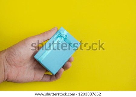 Hand holding blue present box on yellow background