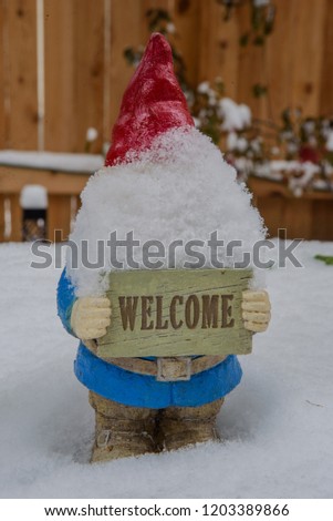 A snow covered gnome holds a welcome sign along a snowy pth