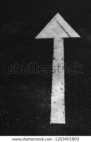 White drawn forward arrow sign on black asphalt road. A guide and direction on the way to  target goals.
