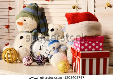 Christmas decorations in festive room. Snowmen, teddy bears, Christmas balls and present boxes near alarm clock. Toys placed on wooden wall background. Celebration and New Year decor concept