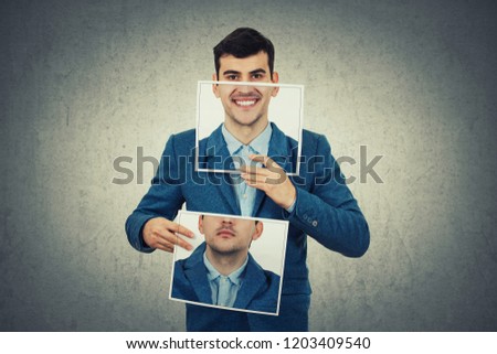 Businessman holding two white photo sheets with different portrait emotions, one hiding half face with angry expression on and another with a happy, smiling face. Switch mask to hide identity concept.