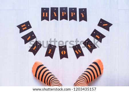 top view of a woman feet with a happy halloween letters on the floor. Woman wearing a black and orange stripes tights. Concept. Indoors and lifestyle