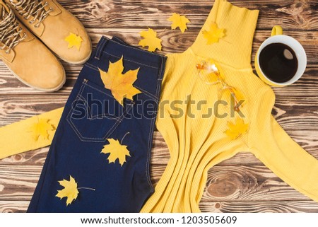 Flatlay of autumn clothes. Top view of woman`s clothes. Sweater, jeans and boots on wooden background