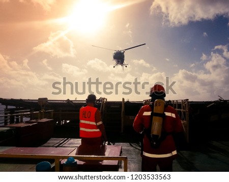 Helicopter landing officer (HLO) and member of a fire team assisting in landing of a helicopter on a offshore drilling rig Royalty-Free Stock Photo #1203533563