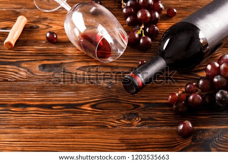 Vintage bottle of red wine with blank matte black label, poured glass, corkscrew & grapes, grunged wood table background. Expensive bottle of cabernet sauvignon concept. Copy space, top view, flat lay
